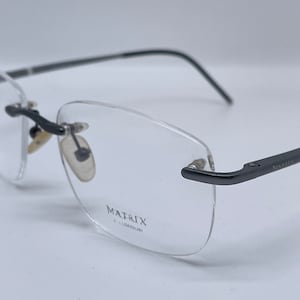 May include: A pair of rimless spectacles with a black metal frame and clear lenses. The frame is labelled "MATRIX ALUMINIUM".