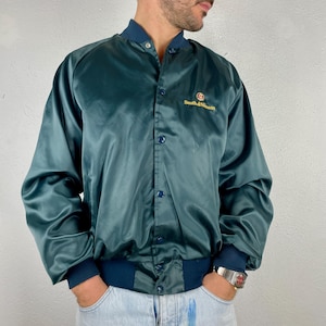 May include: Teal satin bomber jacket with a button-up front, dark blue ribbed collar and cuffs. The jacket features the text "Smith & Wesson" in gold lettering on the chest. The jacket has a classic, vintage style.