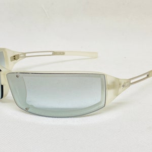 May include: White translucent sunglasses with a silver metal frame and gray lenses. The sunglasses have a lightning bolt logo on the side.