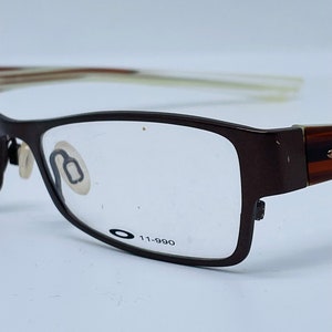 May include: Brown rectangular eyeglasses with clear lenses. The glasses have a dark brown frame with the text "11-990" printed on the lens. The arms of the glasses are a lighter brown color.