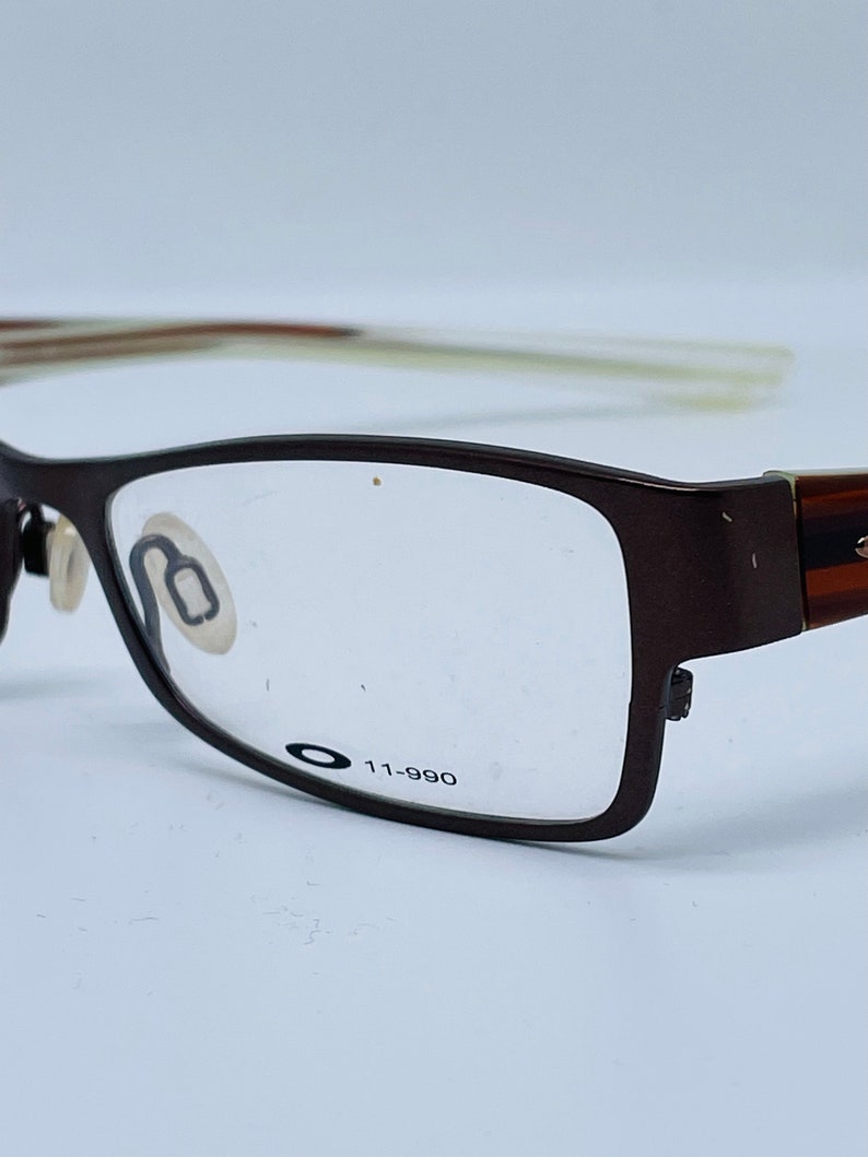 May include: Brown rectangular eyeglasses with clear lenses. The glasses have a dark brown frame with the text "11-990" printed on the lens. The arms of the glasses are a lighter brown color.