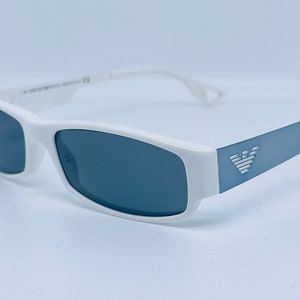 Puede incluir: Gafas de sol rectangulares blancas con lentes grises oscuros y un logotipo azul y plateado en el lateral.