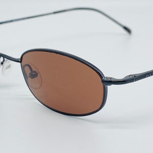 May include: Black oval-shaped sunglasses with brown lenses. The sunglasses have a thin metal frame.