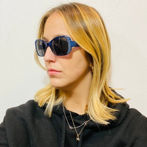 Puede incluir: Una mujer con una sudadera con capucha negra, un collar de estrella dorada y gafas de sol azules con pedrer&iacute;a.