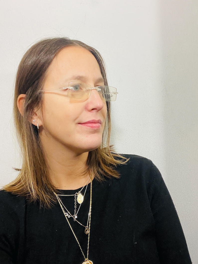 May include: A woman with brown hair wearing clear framed glasses and a black shirt with multiple gold necklaces.