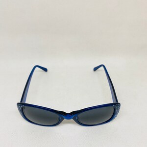 Puede incluir: Gafas de sol azules con pedrer&iacute;a alrededor del marco y lentes oscuras.