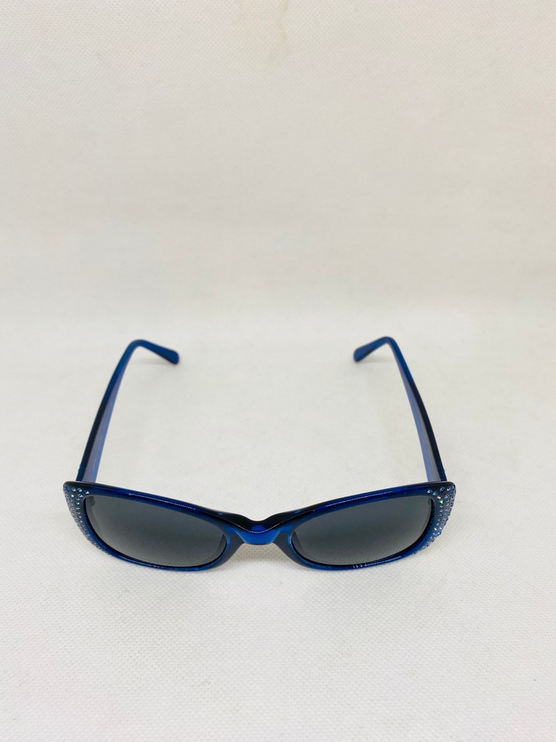 Puede incluir: Gafas de sol azules con pedrer&iacute;a alrededor del marco y lentes oscuras.