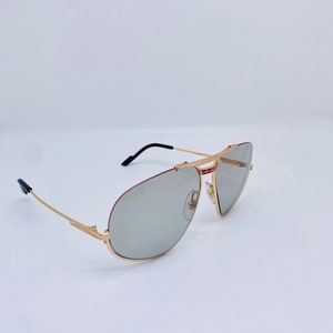 May include: Gold-tone aviator sunglasses with gray lenses and red accents on the frame.