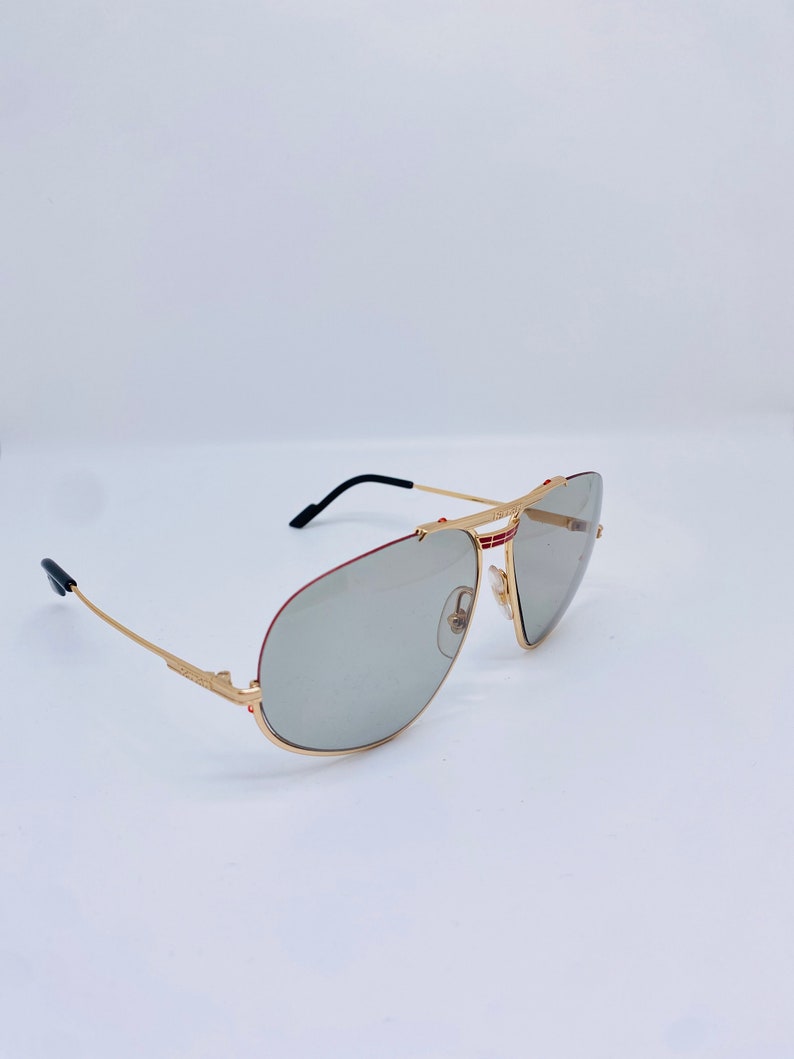May include: Gold-tone aviator sunglasses with gray lenses and red accents on the frame.