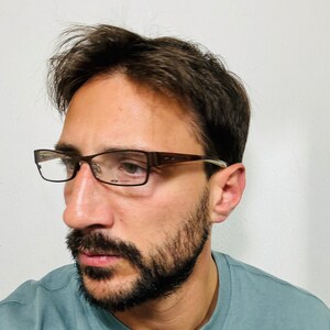 May include: Rectangular eyeglasses with a brown frame and clear lenses. The glasses are worn by a person with a beard and short dark hair. The person is wearing a light blue t-shirt.