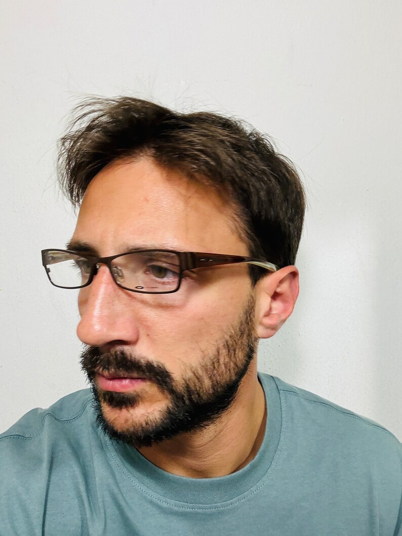 May include: Rectangular eyeglasses with a brown frame and clear lenses. The glasses are worn by a person with a beard and short dark hair. The person is wearing a light blue t-shirt.