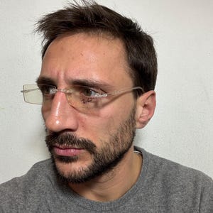 May include: A man wearing a gray sweater and clear framed glasses with the Ray-Ban logo on the right lens.