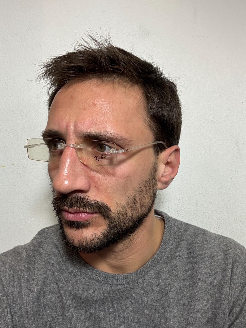 May include: A man wearing a gray sweater and clear framed glasses with the Ray-Ban logo on the right lens.