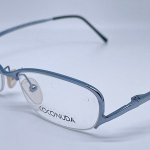 Könnte beinhalten: Blaue Metallgestellbrille mit klaren Gläsern. Der Markenname "COCONUDA" ist auf dem rechten Glas aufgedruckt.