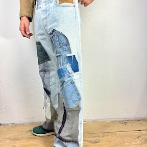May include: Light blue denim jeans with multiple patches of different coloured denim sewn on. The jeans have a distressed look with some rips and tears.