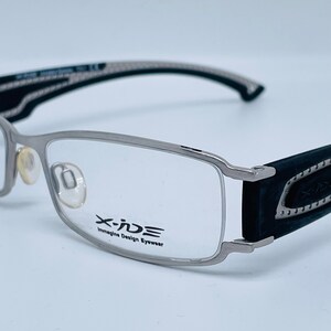 Pode incluir: Óculos X-IDE Imagine Design Eyewear em prata e preto com ponta da haste de borracha preta.