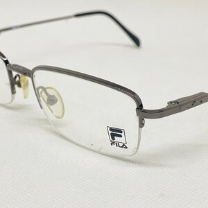 May include: A pair of silver-toned metal frame spectacles with clear lenses. The brand name "FILA" is printed on the right lens.