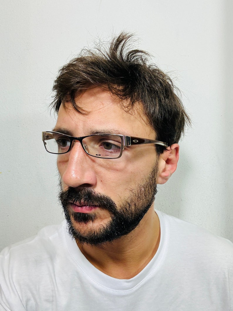 Może przedstawiać: Mężczyzna z brązowymi włosami i brodą nosi okulary w brązowej oprawce. Ma na sobie biały t-shirt.