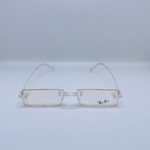 May include: Clear frame glasses with a light brown lens and Ray-Ban branding on the right temple.