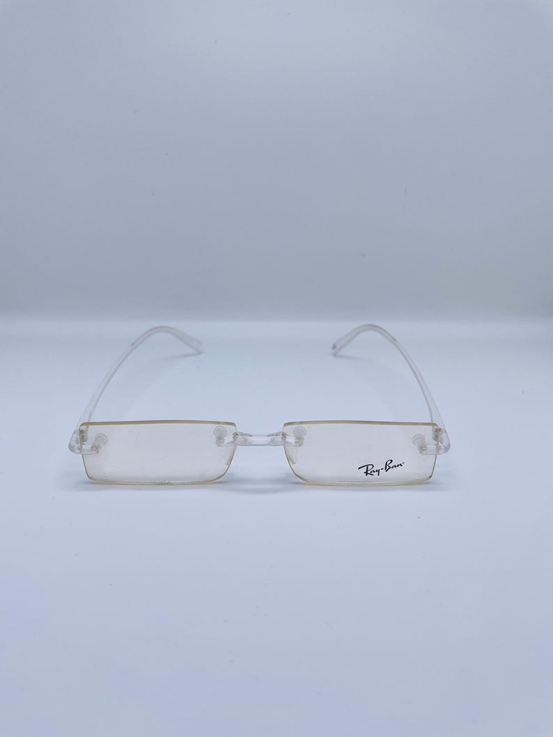 May include: Clear frame glasses with a light brown lens and Ray-Ban branding on the right temple.