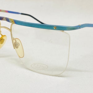 Puede incluir: Un par de gafas de color azul y dorado con lentes transparentes. Las gafas tienen un diseño angular único y el nombre de la marca "REPS" está impreso en la montura.