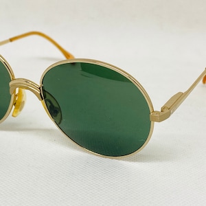 Può includere: Occhiali da sole rotondi dorati con lenti verde scuro.