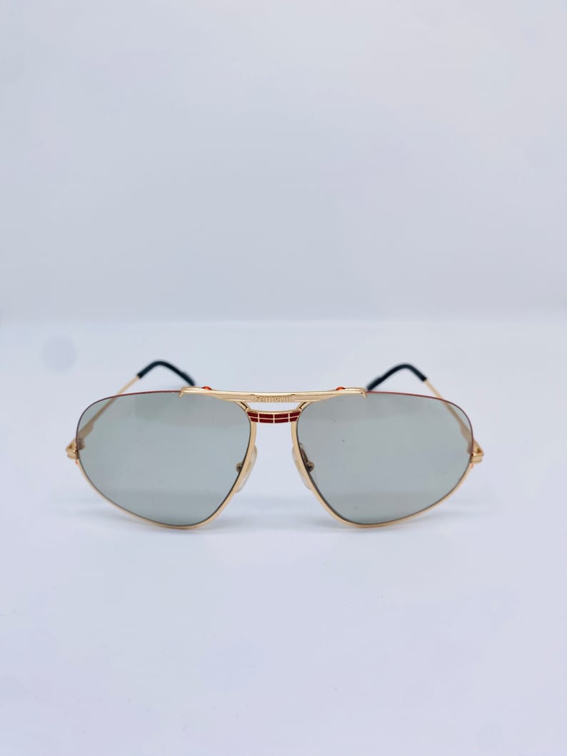 May include: Gold aviator sunglasses with gray lenses and a red and black stripe detail on the frame.