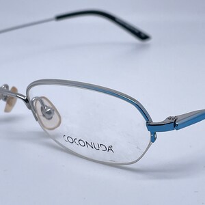 Könnte beinhalten: Silberne und blaue randlose Brille mit dem Markennamen "COCONUDA" auf dem Rahmen.