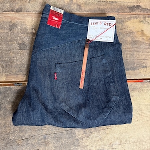 Könnte beinhalten: Dunkelblaue Jeans mit einem roten Etikett mit der Aufschrift "RED" und einem weißen Etikett mit der Aufschrift "LEVI'S RED Copper Riveted". Die Jeans haben ein klassisches Fünf-Taschen-Design und ein rotes Levi's-Logo auf der Gesäßtasche. Bundweite 91 cm.