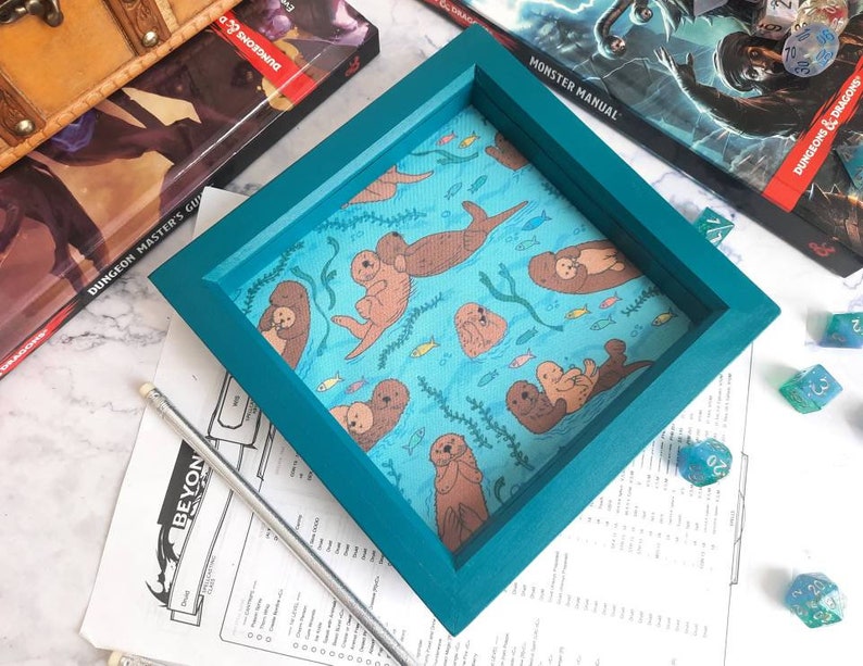 May include: Teal blue wooden dice tray with a light blue fabric insert featuring a repeating pattern of sea otters and fish.