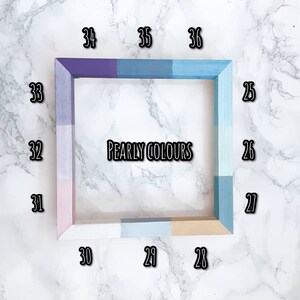 May include: A wooden frame with 36 different shades of paint, labeled with numbers 28 through 36. The frame is on a white marble surface. The text "PEARLY COLORS" is printed in black inside the frame.