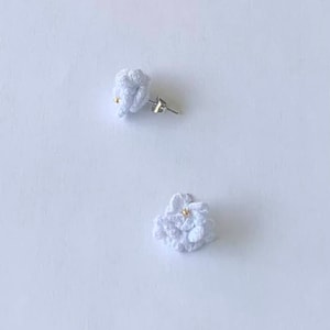 Op de afbeelding: Een paar witte gehaakte bloemoorbellen met gouden accenten.