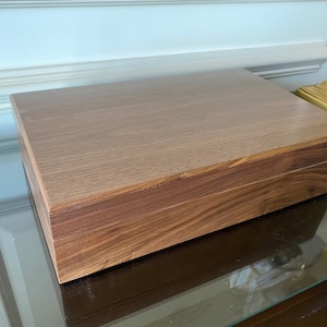 Może przedstawiać: Drewniana skrzynia z jasnobrązowym wierzchem i ciemnobrązowym dnem. Skrzynia ma gładkie, polerowane wykończenie.