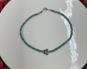 Peut inclure: Un collier délicat de perles vertes avec un pendentif en forme d'étoile. Le collier est sur une assiette blanche avec une bordure de fraises rouges.