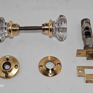 May include: A set of antique brass door hardware with clear glass knobs. The set includes two knobs, two rosettes, a latch, and a strike plate. The latch is marked "Dexter".