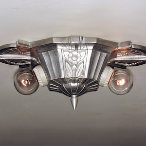 May include: A silver ceiling light fixture with two light bulbs. The fixture has a geometric design with a central point and decorative details.