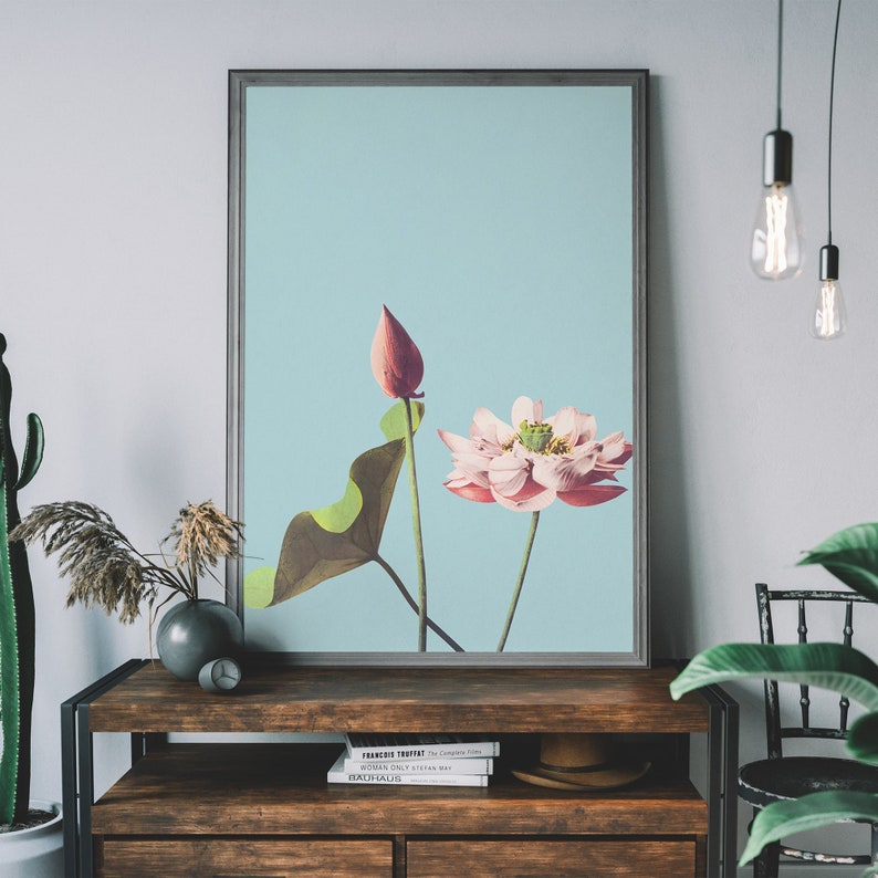May include: A framed print of a pink and white lotus flower with a green leaf and a single bud on a light blue background.