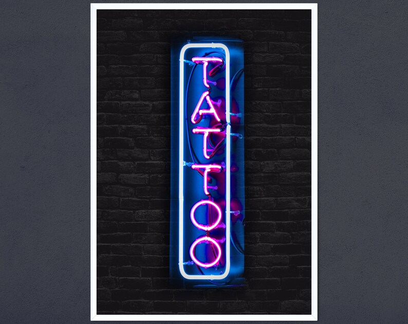 May include: A neon sign with the word "TATTOO" in pink letters on a blue background. The sign is mounted on a brick wall.