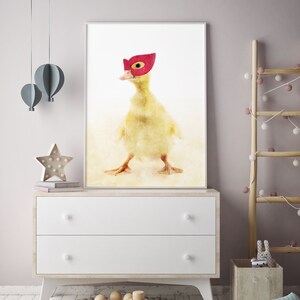 May include: A watercolour painting of a yellow duckling wearing a red superhero mask. The duckling is standing on a light brown background.