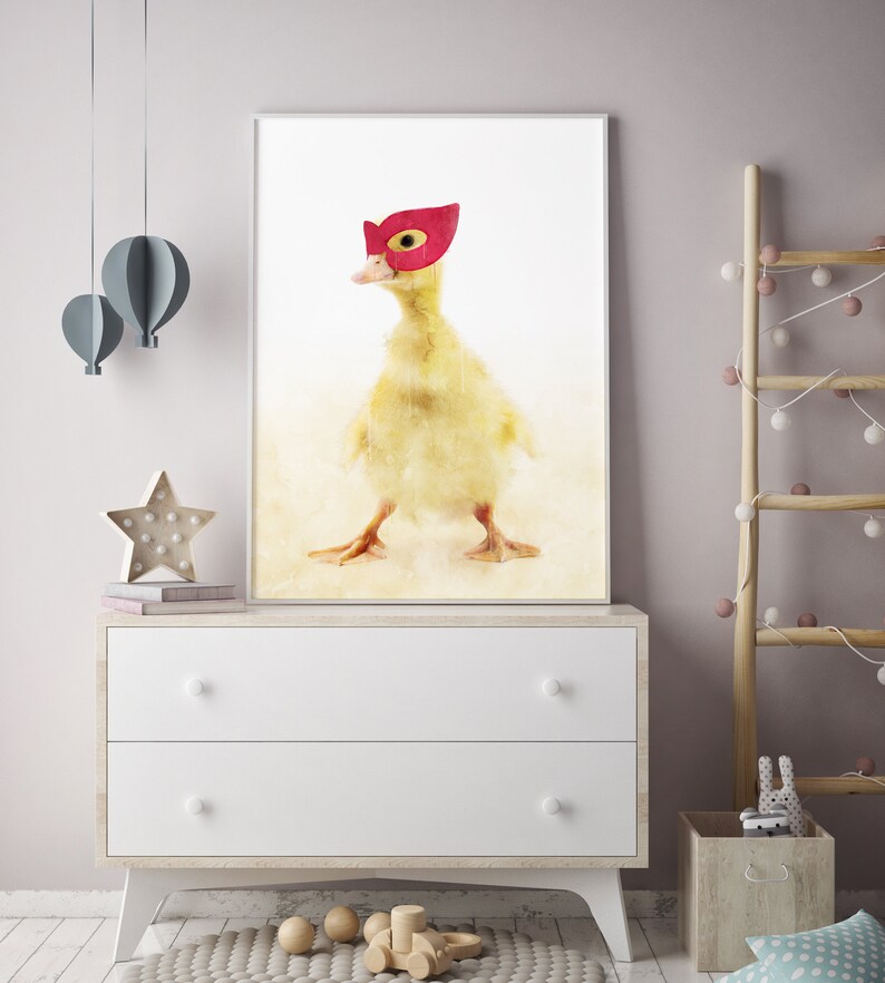May include: A watercolour painting of a yellow duckling wearing a red superhero mask. The duckling is standing on a light brown background.