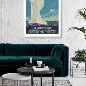 May include: A vintage travel poster for Yellowstone National Park, featuring a geyser erupting against a blue sky with white clouds. The poster is framed in white and has text that reads "Ranger Naturalist Service" and "Yellowstone National Park".