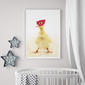 May include: A yellow duckling wearing a red superhero mask. The duckling is standing on a white background.