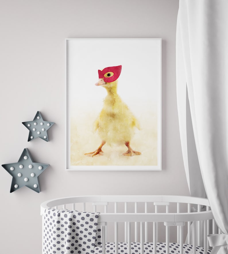 May include: A yellow duckling wearing a red superhero mask. The duckling is standing on a white background.