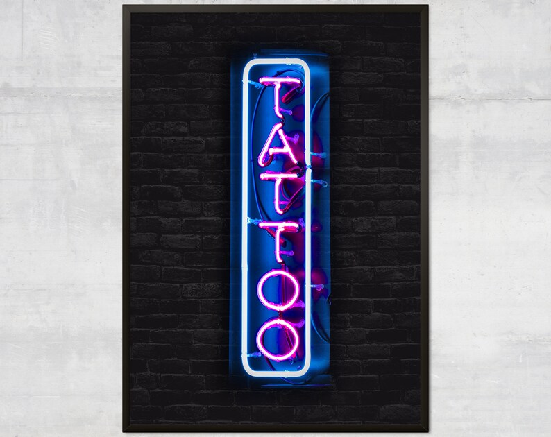 May include: A neon sign with the word "TATTOO" in white letters with a pink outline against a dark brick wall background.