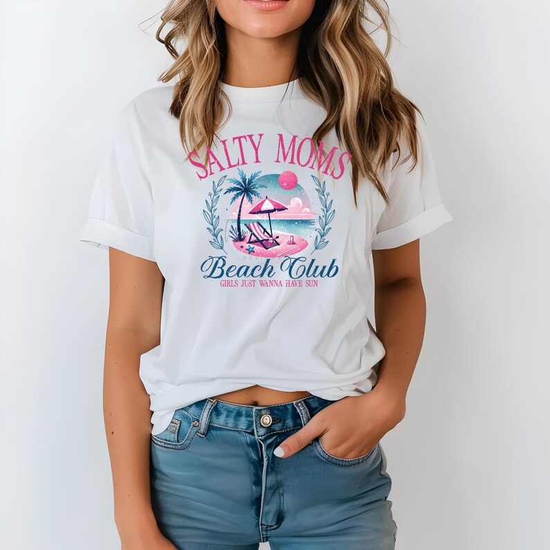 Op de afbeelding: Wit T-shirt met een roze en blauw grafisch ontwerp met de tekst "Salty Moms Beach Club Girls Just Wanna Have Sun".
