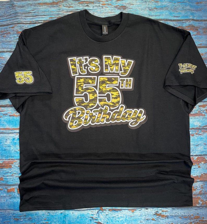 May include: Black t-shirt with the text "It's My 55th Birthday" in a yellow and black camouflage design. The number 55 is also on the left sleeve. A small logo is on the right sleeve.