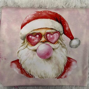May include: A pink graphic featuring Santa Claus wearing heart-shaped sunglasses and blowing a bubble. Santa's red hat and suit contrast with his white beard and the pink bubblegum. The design is on a pink background.