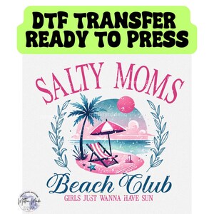 Op de afbeelding: Een roze en blauw grafisch ontwerp met de tekst "Salty Moms Beach Club" en de woorden "Girls Just Wanna Have Sun". Het ontwerp toont een strandscene met een palmboom, een strandstoel en een parasol.