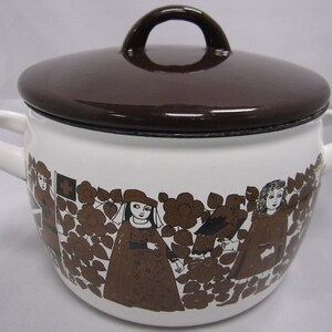 May include: White enamel pot with a brown lid and handle. The pot features a brown floral and figure design around the base. The pot has two white handles on either side.