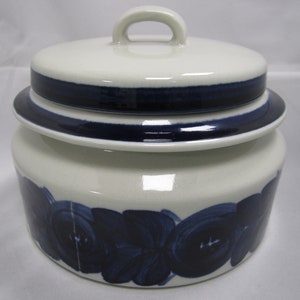 May include: A white ceramic jar with a blue and white floral design and a lid with a handle. The jar has a blue band around the top and bottom.